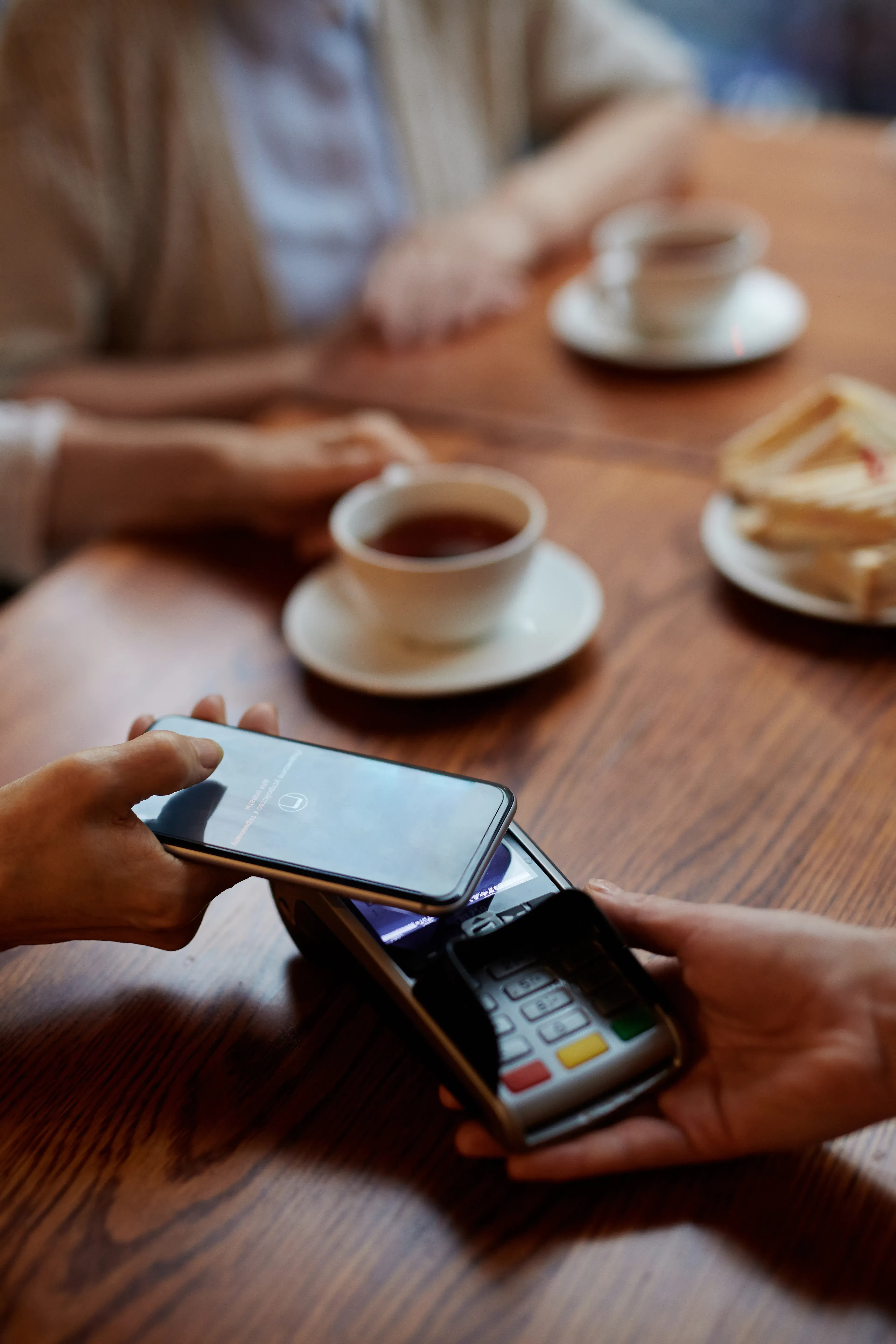A smartphone is held up to a reader in a café so that you can make a contactless payment.