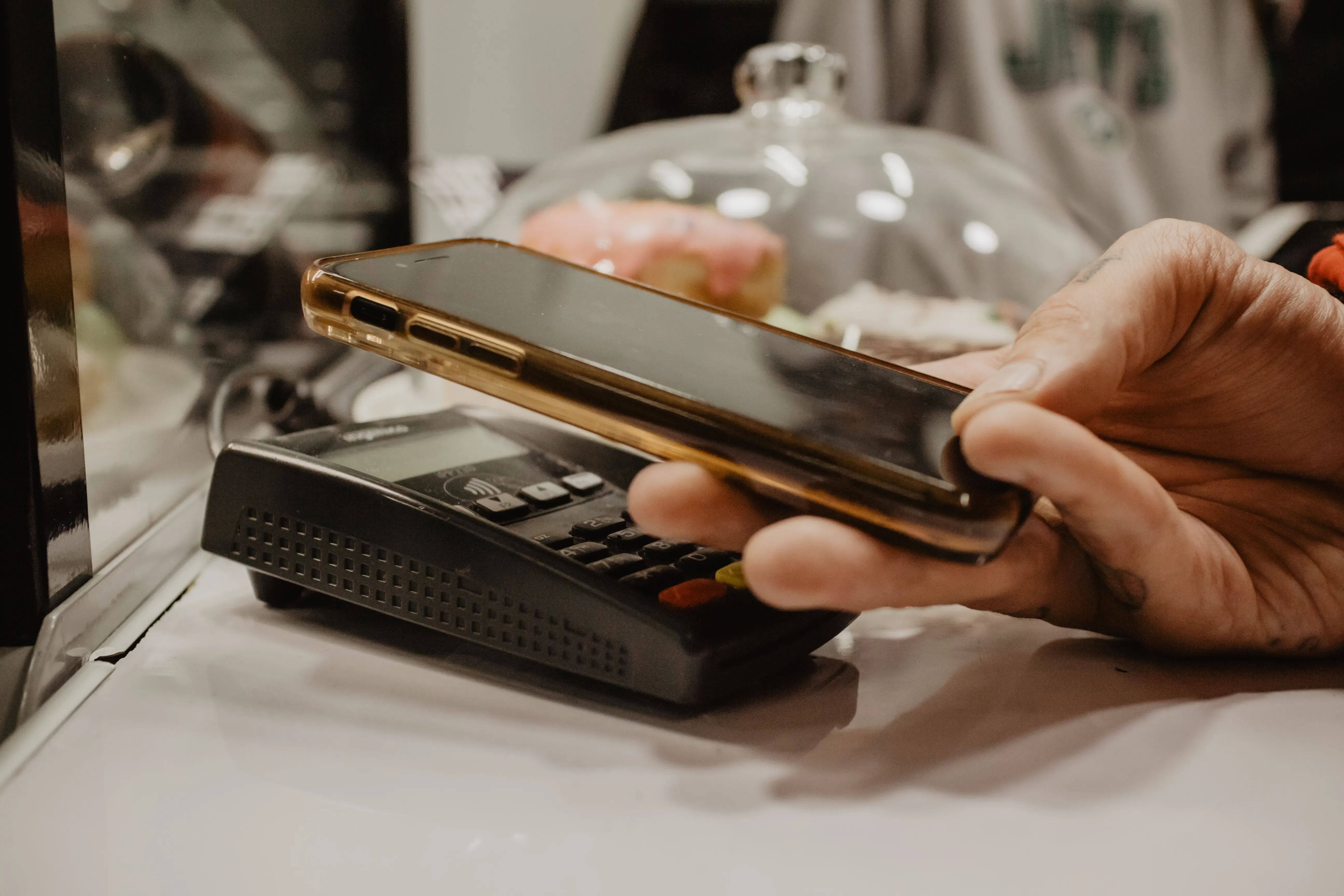 A smartphone is held up to a reader in a café so that you can make a contactless payment. The NFC symbol is visible on the reader.