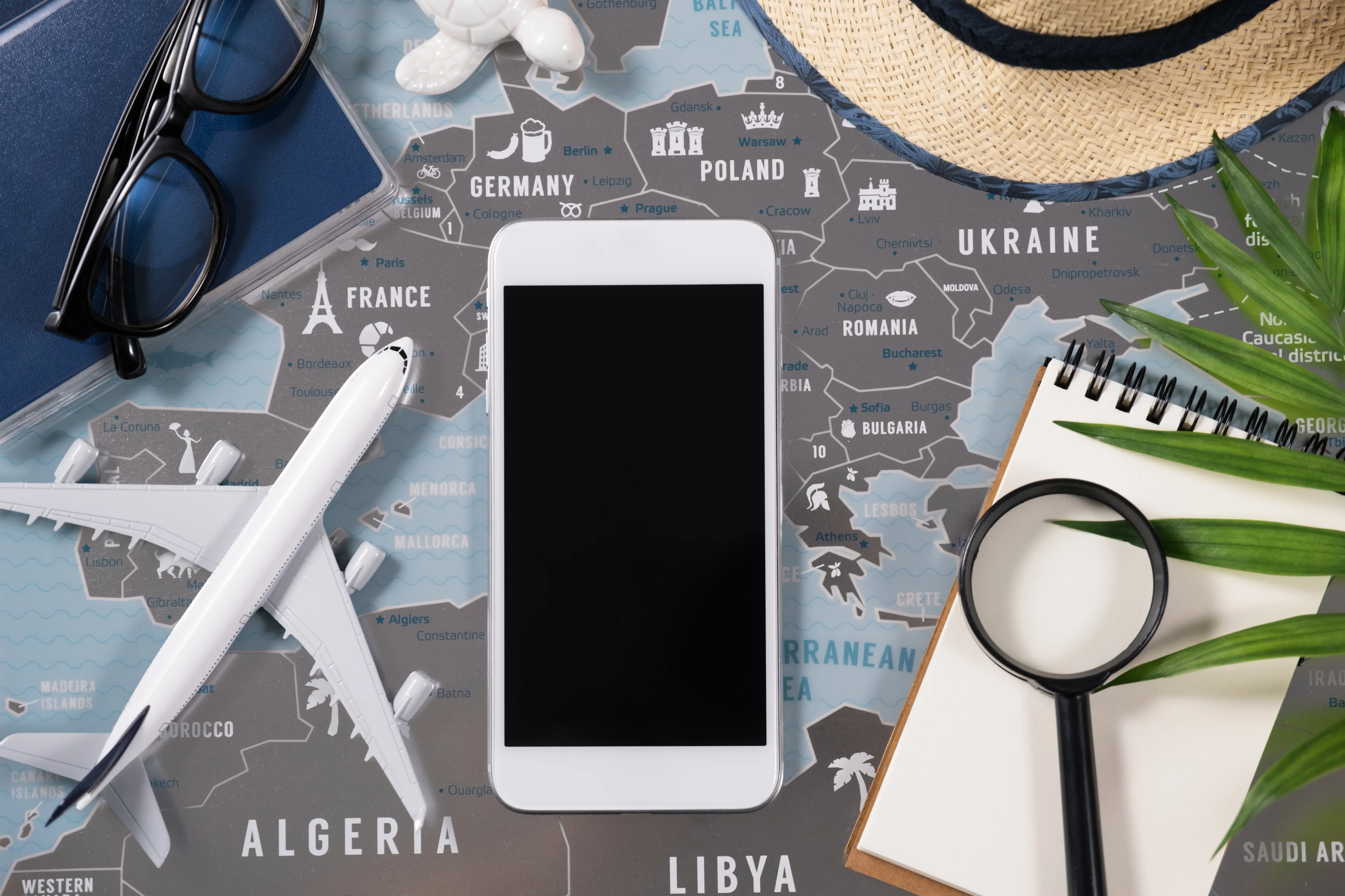 Ein Smartphone liegt auf einer Weltkarte und ist von Reiseutensilien umgehen.